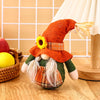 Thanksgiving gnome doll with orange hat and sunflower decoration on a wooden table with harvest-themed background.