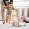 Toddler using a wooden baby walker push toy with ABC blocks for learning and balance, supported by a parent in a cozy room.