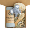 Baby teething toy gift set with gauze blanket, elephant toy, wooden brush, teething ring, and milestone disc in a box.