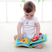 Baby playing with a colorful soft cloth book, enhancing learning with interactive features like zippers and buttons.