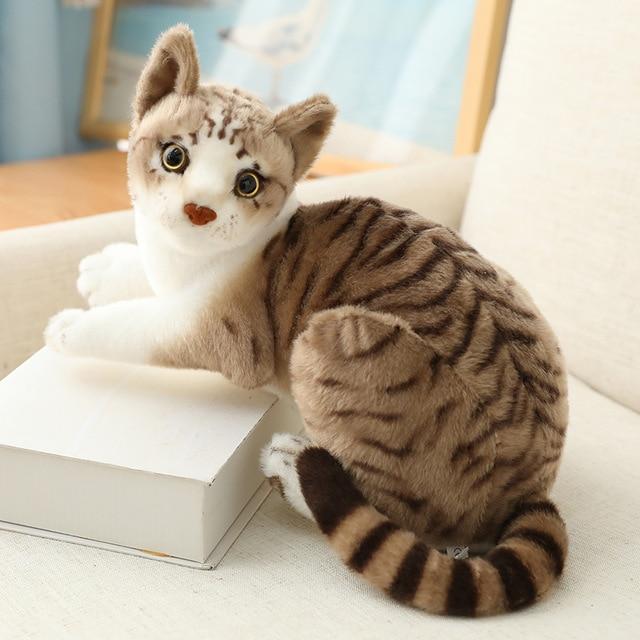 Soft cat plush toy with realistic design sitting on a white book, perfect for gifts and home décor.