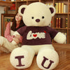 Giant teddy bear plush with "Love" shirt, perfect for Valentine's Day gift, woman sitting beside it for scale.