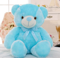 Blue LED teddy bear with bow on decorated bed, part of Glowing LED Teddy Bear collection, providing comfort and colorful light for kids.