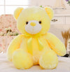 Yellow plush teddy bear with a satin bow on a bed, perfect for children's décor and gift ideas.