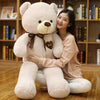 Woman hugging a large plush teddy bear doll with a ribbon design, perfect for cuddling and gifting.