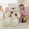 Giant plush teddy bear with ribbon, sitting beside a person in a cozy room.