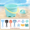 Kids beach toy set with pastel bucket, watering can, and colorful shovels on sand with ocean background.