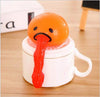 Funny vomiting egg yolk toy with orange head and red yolk on a white mug, perfect for stress relief and pranks.