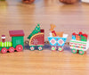 Mini wooden Christmas train set with festive designs, including Christmas tree, reindeer, and gift-filled carts on a wooden surface.