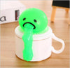 Green vomiting egg yolk toy sitting on a mug, perfect for stress relief and pranks, with a quirky and hilarious design.