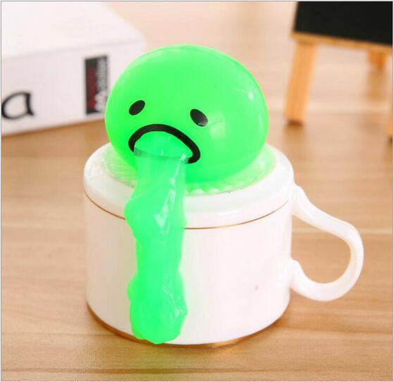 Green vomiting egg yolk toy sitting on a mug, perfect for stress relief and pranks, with a quirky and hilarious design.