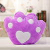 Plush purple paw-shaped pillow with white heart design on a cozy room background.