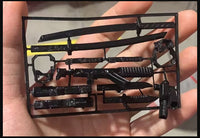 Hand holding a black plastic model kit showing miniature weapons for 3D-printed robot action figure assembly.