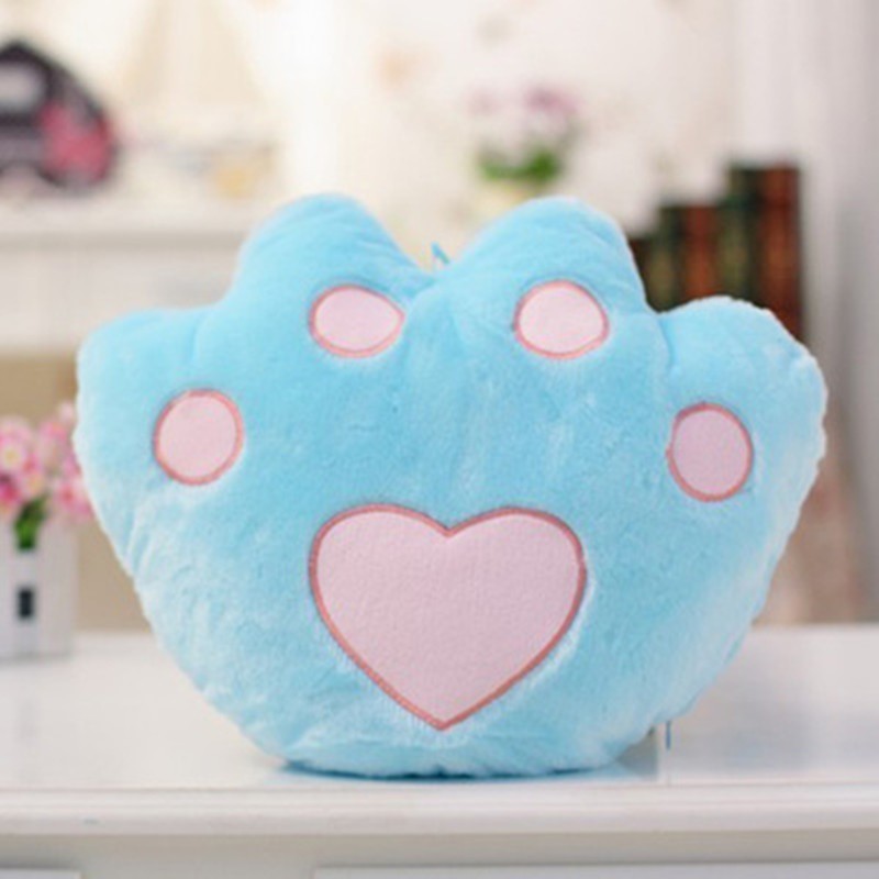 Blue plush paw pillow with pink heart and padded paws on a shelf background.