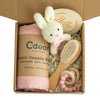 Baby teething gift set with muslin swaddle, wooden brush, teether rings, and knitted bunny toy in a cozy box.