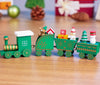 Mini wooden Christmas train set with festive designs on tabletop featuring trees and snowmen. Perfect holiday décor ornament.