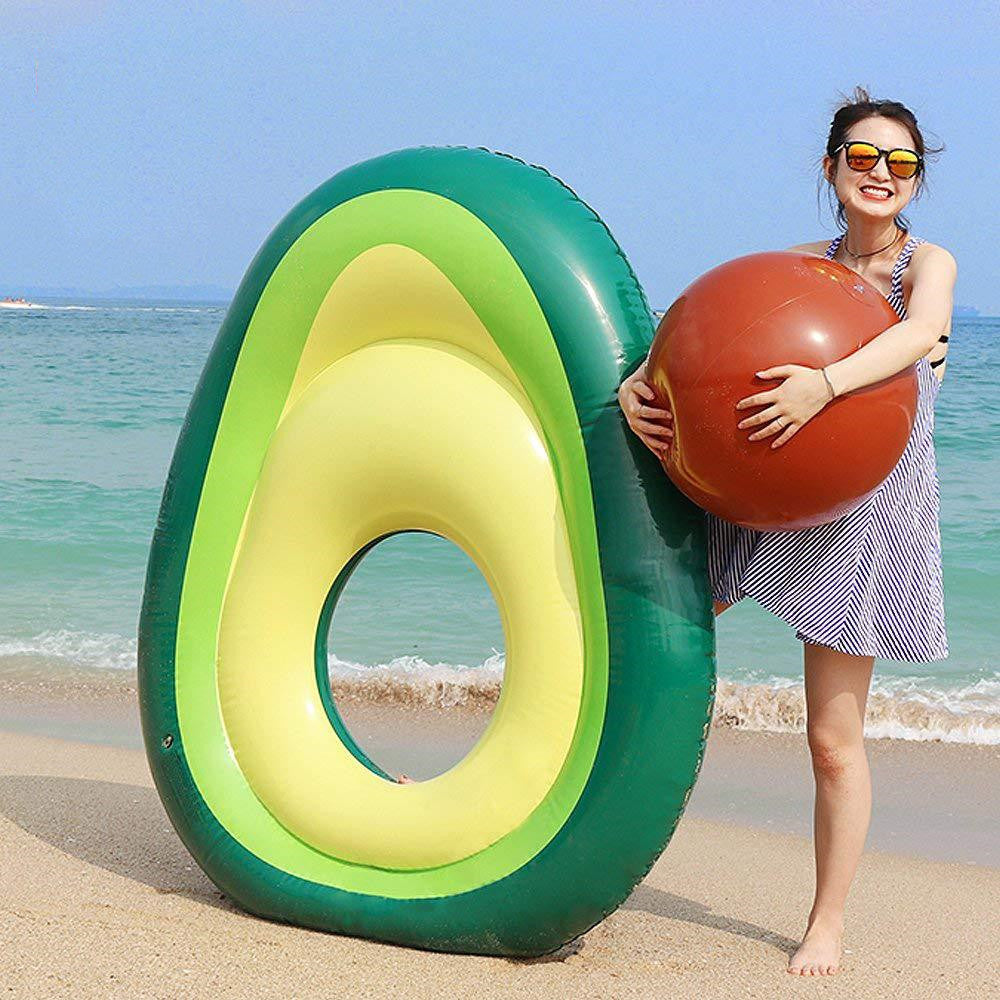 Giant inflatable avocado pool float at the beach with person holding an inflatable pit.