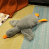 Gray plush goose doll pillow with orange beak and feet on a colorful rug, perfect for cuddling and decoration.