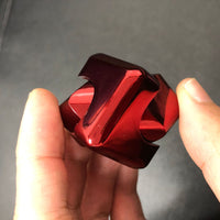 Hand holding a red metal fidget spinner, showing its shiny, smooth surface and unique geometric design for stress relief.