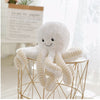 Adorable baby octopus plush toy with smiling face on table, perfect for cuddling and nursery decor.