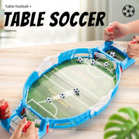 Mini tabletop soccer game with blue edges, being played by two hands, includes four soccer balls and green field design.