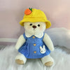 Little Bear Plush Doll dressed in blue with changeable clothes and a yellow hat, sitting on a soft surface.