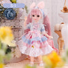 Articulated 1/6 BJD doll in a pink and blue dress with accessories, standing in a floral setting for dress-up play.