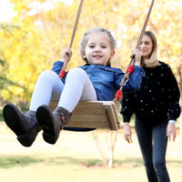 Child enjoying a ride on a wooden hanging swing seat outdoors with a woman pushing, highlighting fun and playtime.