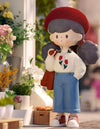 Retro Molinta Girl figurine in garden with red hat and blue pants, surrounded by colorful flowers.