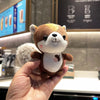 Hand holding a kawaii squirrel plush toy with a cute, colorful design in a cafe setting.