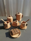 Wooden pretend play kitchen set with cups, sugar bowl, cake slice, and chocolate bar on a table for children's role play.