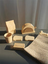 Wooden pretend play kitchen accessories including toy milk carton, toast, butter, and a woven placemat set on a table.