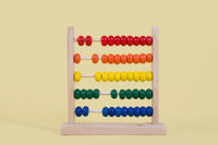 Colorful wooden abacus with red, orange, yellow, green, and blue beads on a pastel yellow background.