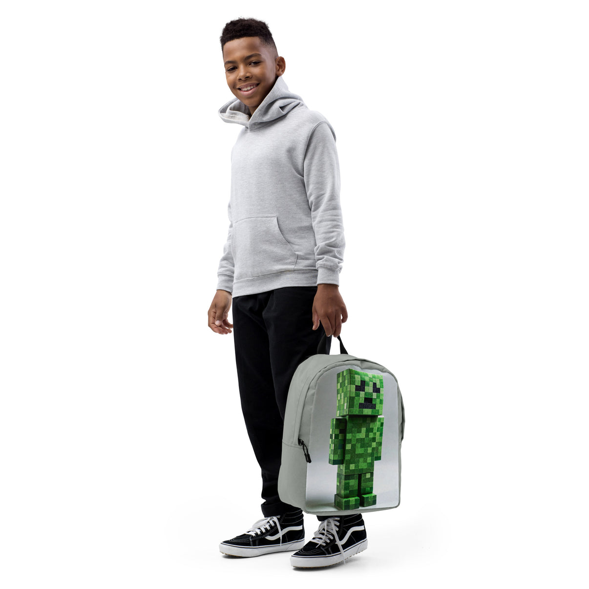 Teen holding a minimalist backpack with bold Minecraft Creeper art, wearing casual attire, showcasing the bag's gaming style and practicality.