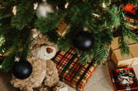 Christmas gifts and teddy bear under a decorated tree with black ornaments.