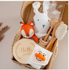 Baby gift set with teething toys, soft cloth, wooden brush, and plush animals in a woven basket for sensory development.