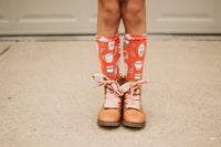 Child wearing orange socks with coffee cup designs and brown boots standing on a concrete path.