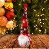 Children's festival decoration doll with a tall red hat and fabric candy jar, set against a festive background with lights and ornaments.