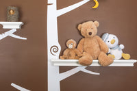 Plush teddy, monkey, and penguin toys sitting on shelves against a brown and white nursery wall with tree design.